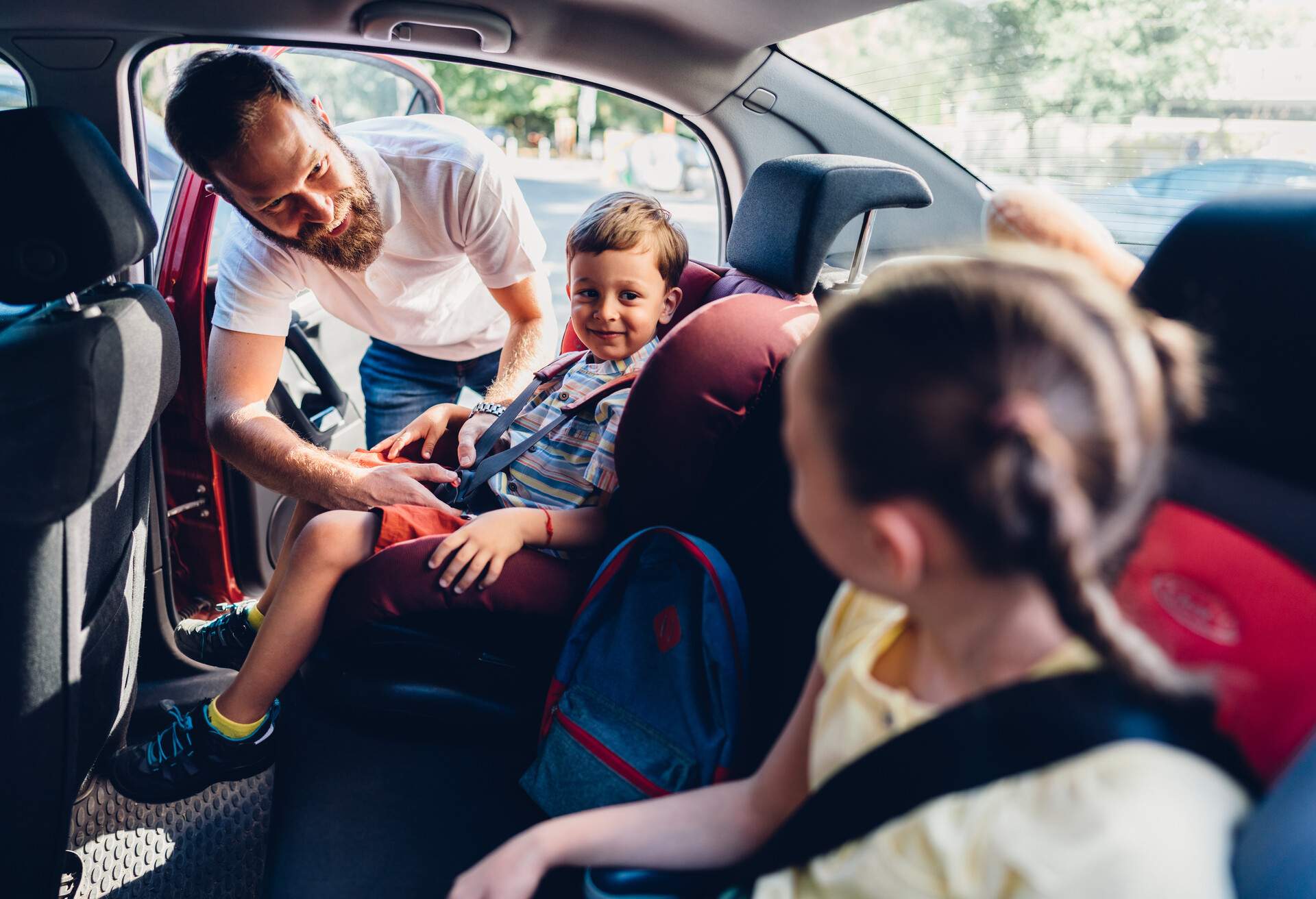 A father getting his kids into their booster seats in the car before the trip.