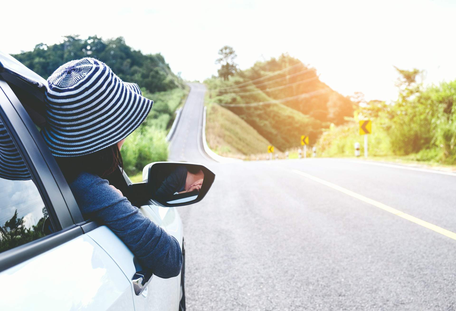 Woman with hat peering outside car on a road trip. 