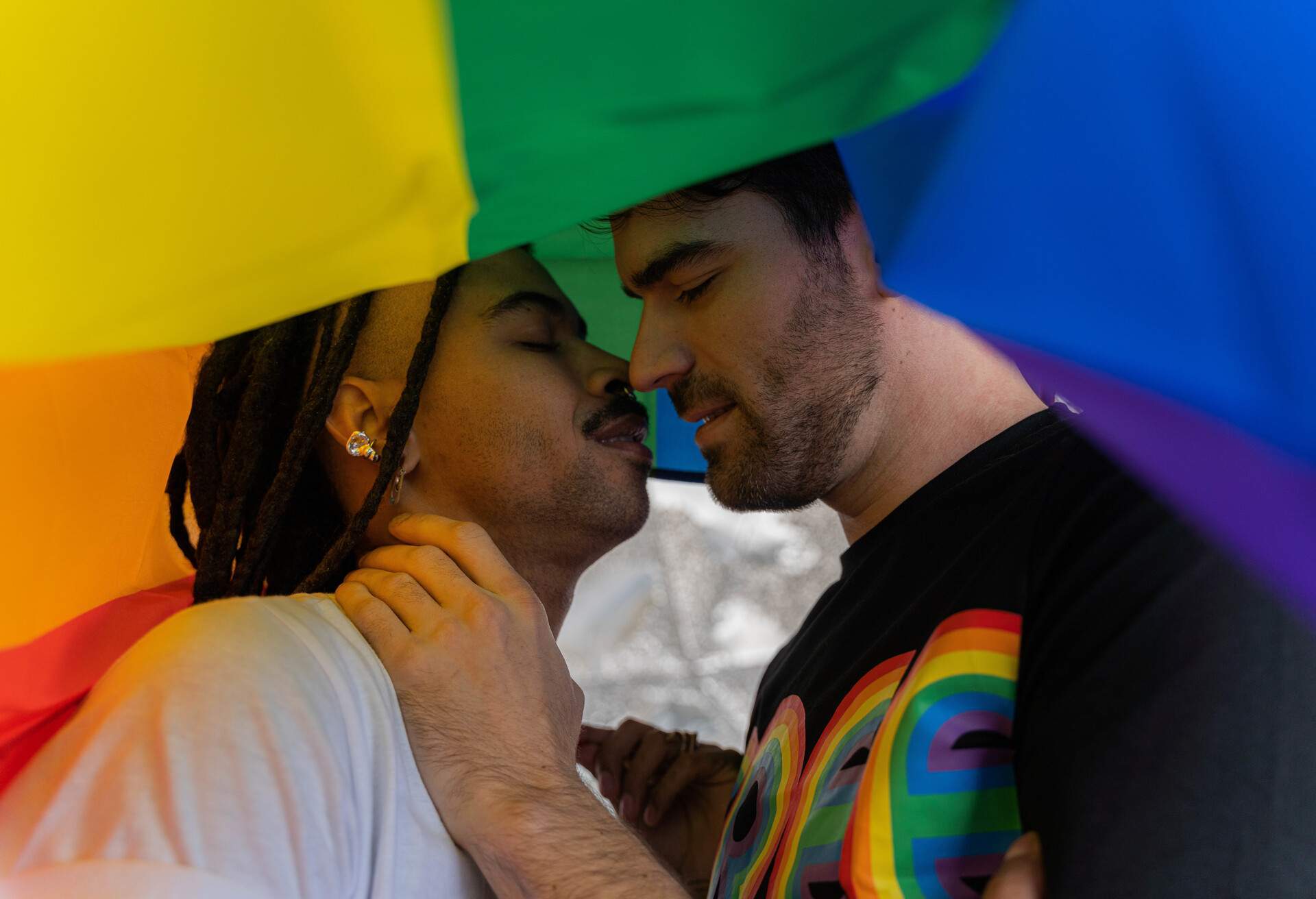 A gay couple poised to kiss under the pride flag.