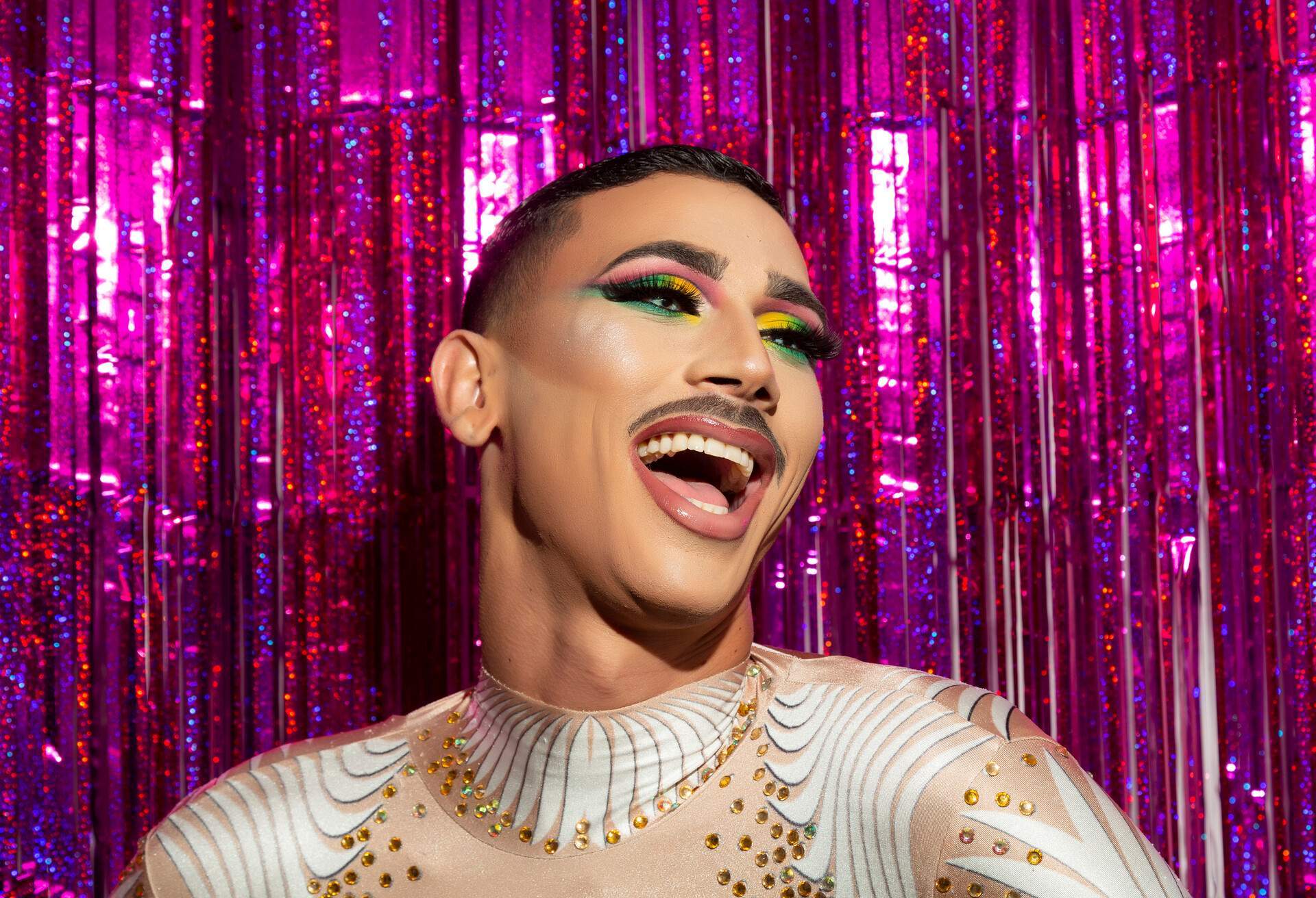 young gay man with makeup happy smiling with a colorful background 