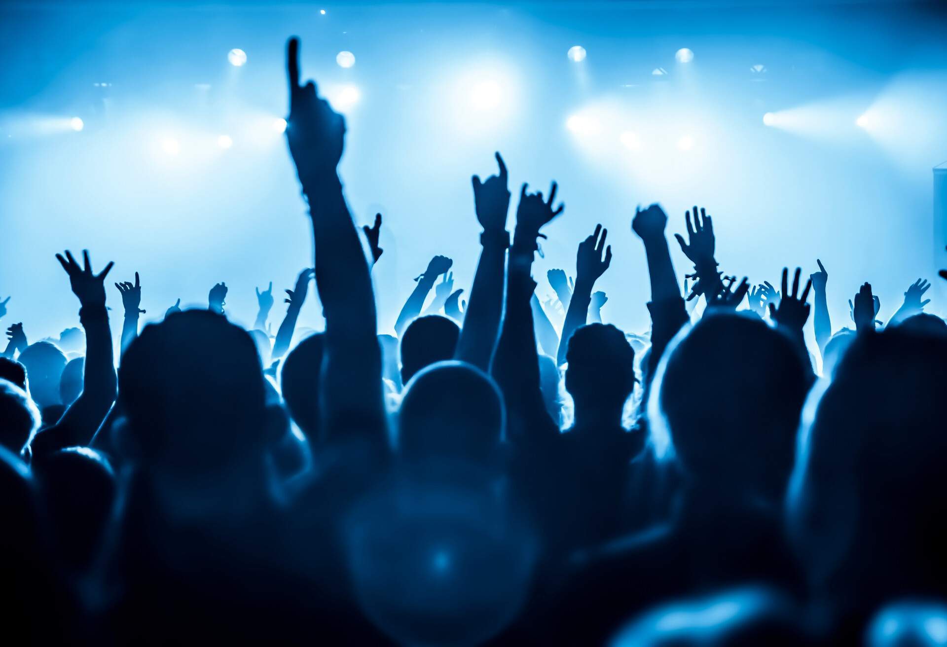 Silhouette of people raising their hands in the air against the glaring stage lights.