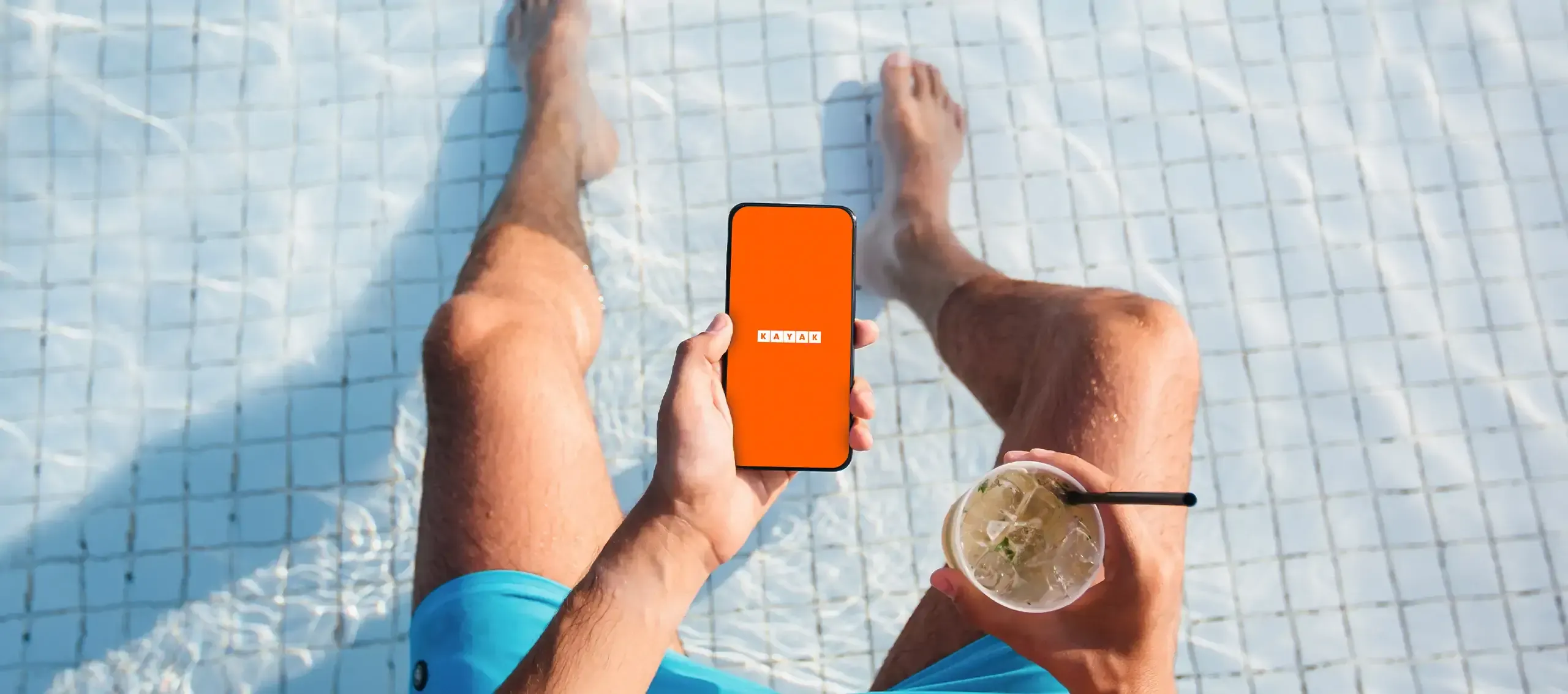 Relaxing poolside with a drink and the KAYAK app open on a smartphone.