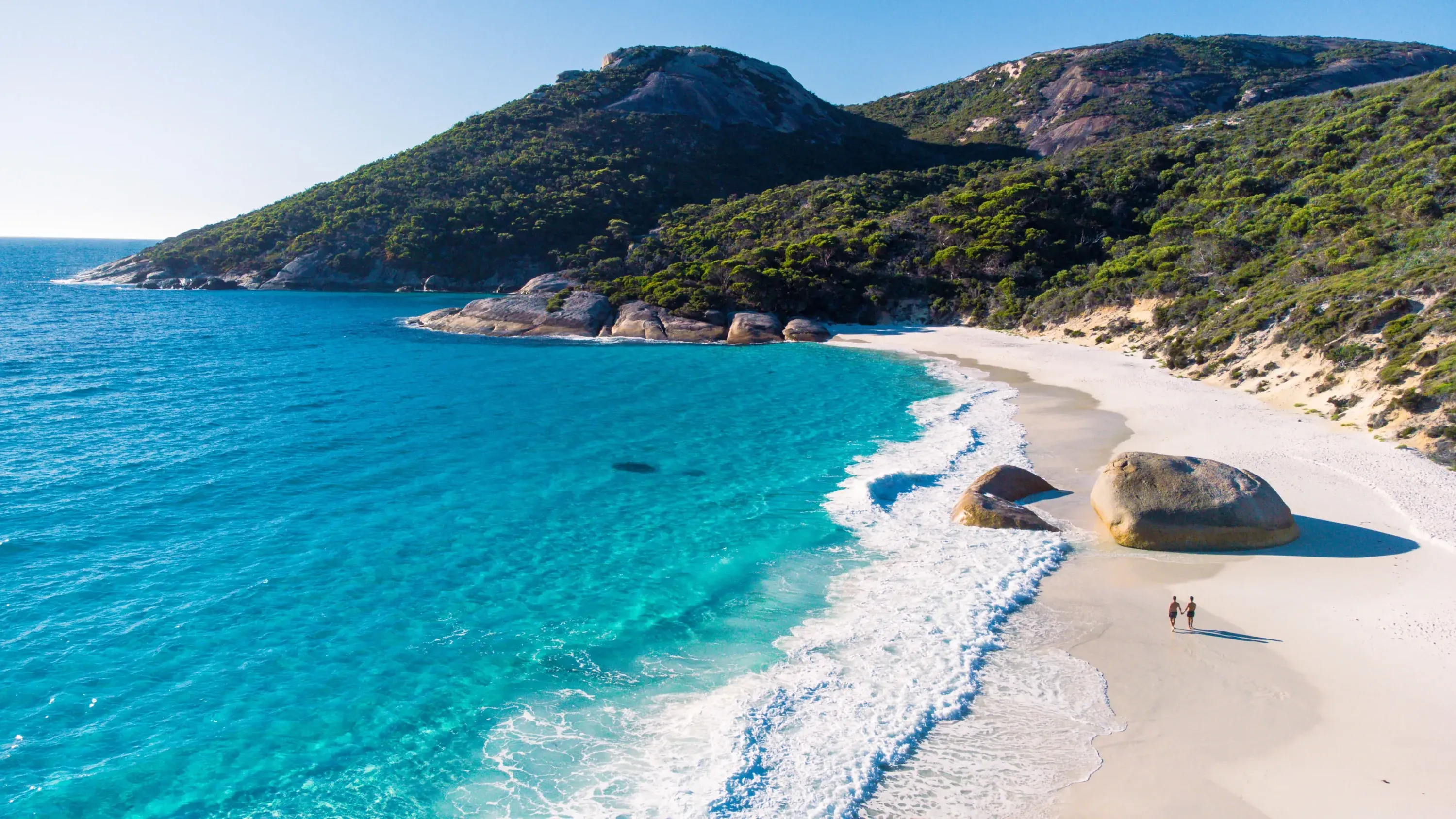 A pristine, secluded beach with brilliant turquoise water, white sand, and a lush green hill.