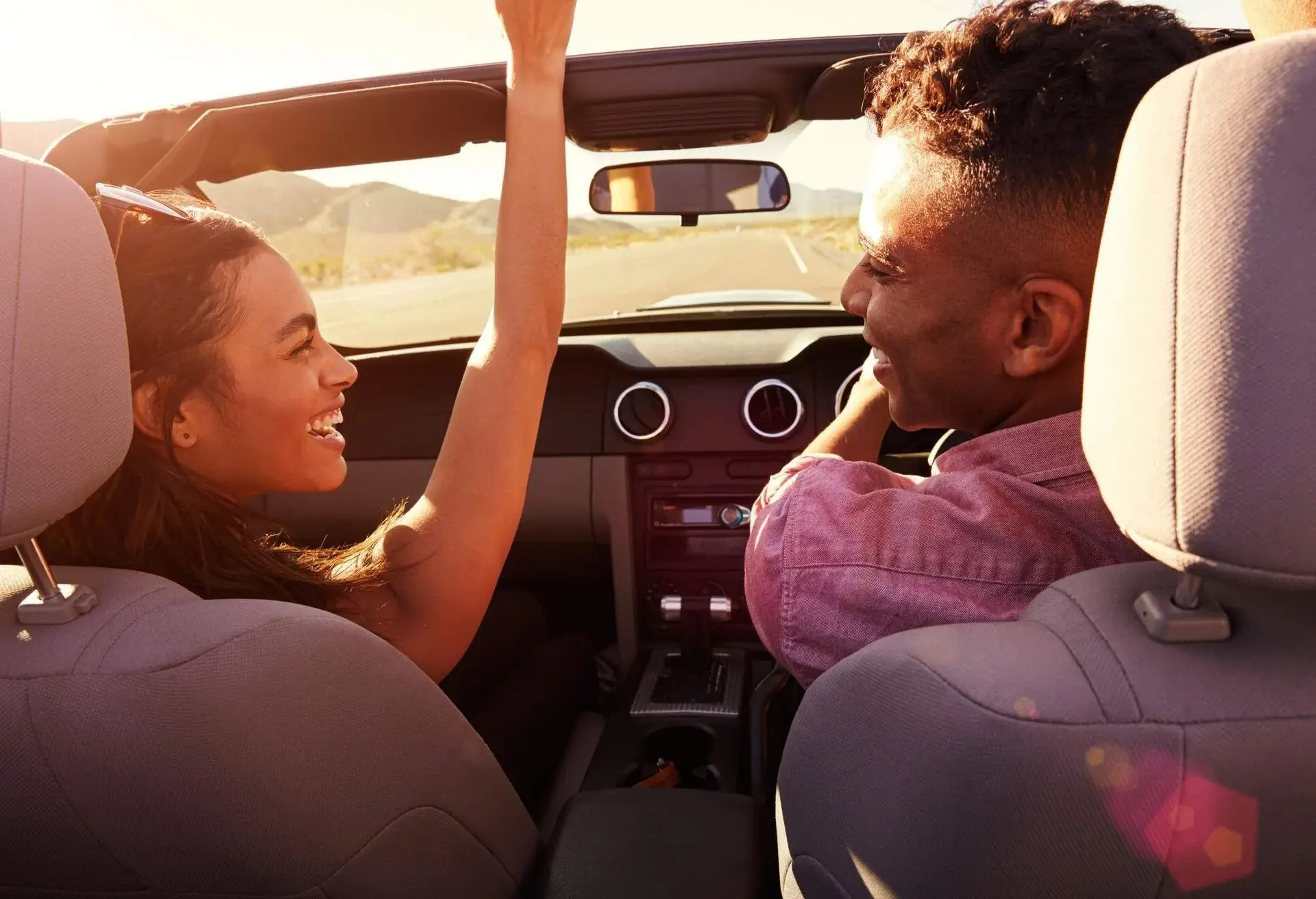 A couple smiles at each other as they sit inside a convertible car.