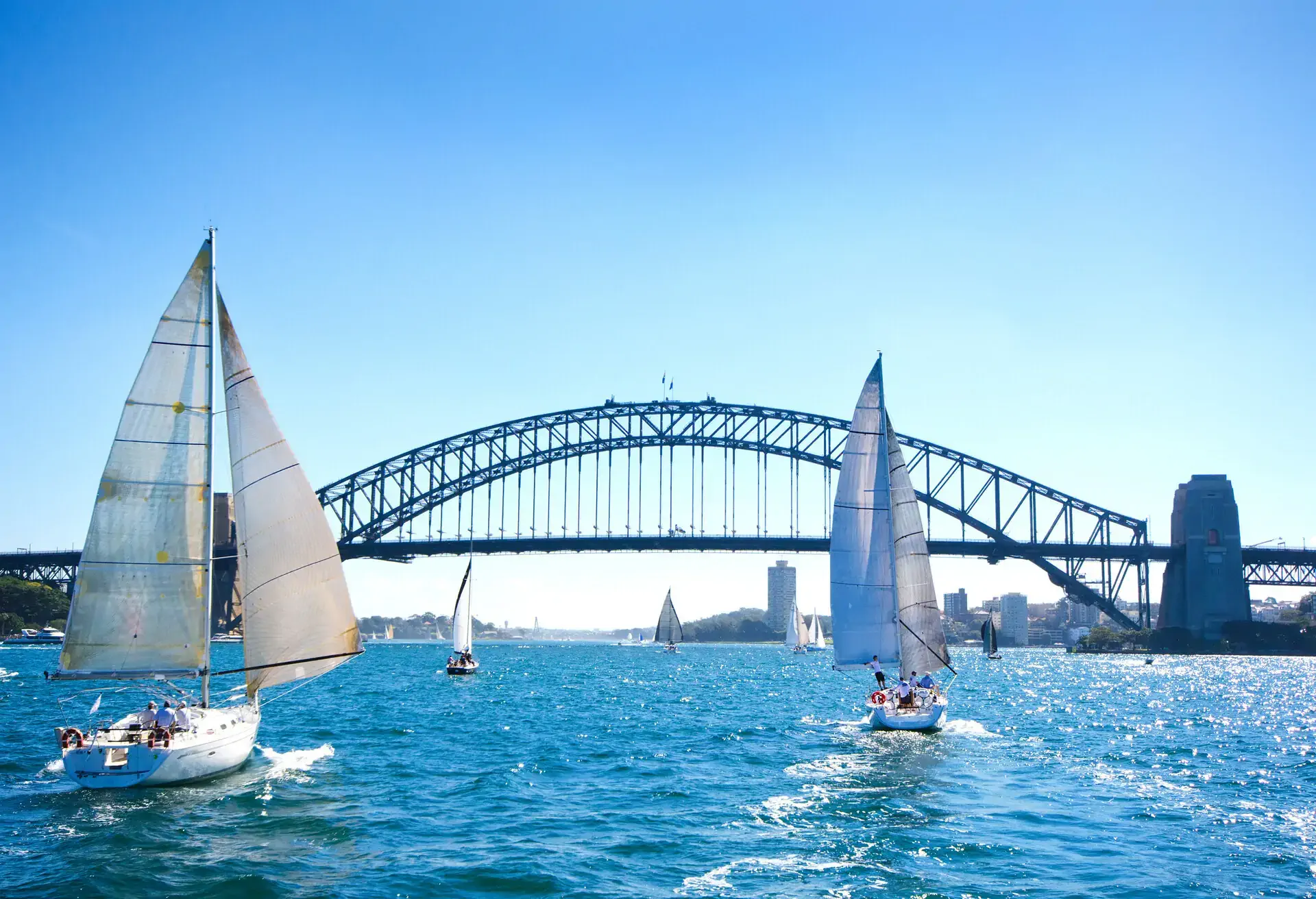 Sailboats on a sunny day at Sydney Harbor, Australia.   Iconic Sydney Harbor Bridge in the background.  Blue tint applied to enhance the sunny blue sky day.